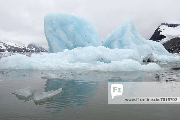 Eisberg spiegelt sich an bewölktem Tag im Wasser der Bucht Samarinvågen im Hornsund