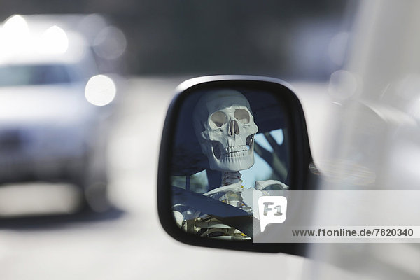 Skeleton at the wheel of a car  skull reflected in the wing mirror of a car