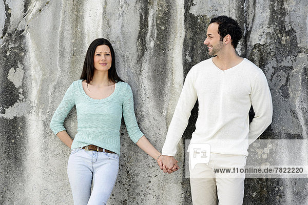 Junges Paar steht Hand in Hand an einer Wand