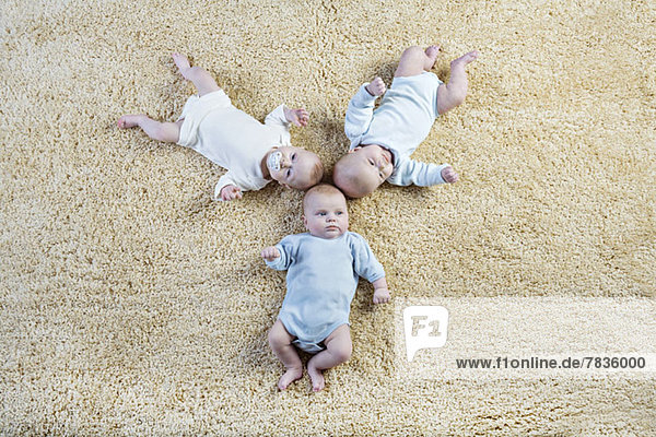 Bildung von drei Babys  die auf einem Teppich liegen.