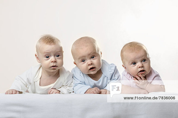 Drei Babys hintereinander ziehen lustige Gesichter.