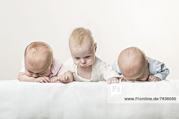 Drei Babys hintereinander ziehen lustige Gesichter.