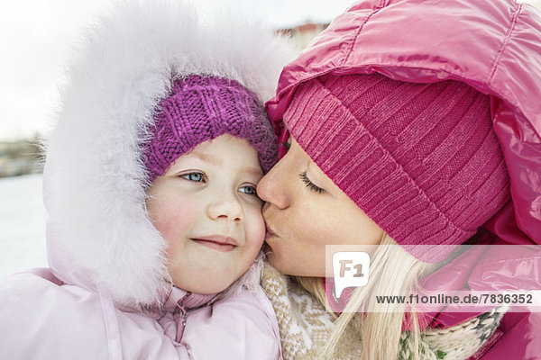 A mother kissing her daughter outdoors in winter