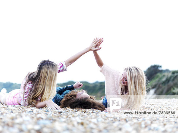 A girl lying in between two friends high-fiving above her at the beach