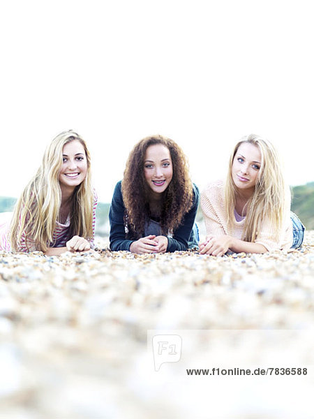 Three cheerfully smiling friends lying on a rocky beach