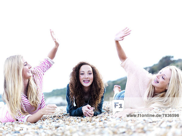 A girl lying in between two friends high-fiving above her at the beach