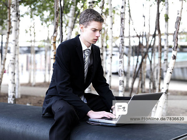 Ein junger Geschäftsmann  der einen Laptop in einem Stadtpark benutzt.
