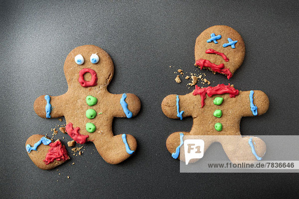 A shocked gingerbread man with broken leg next to a decapitated gingerbread man