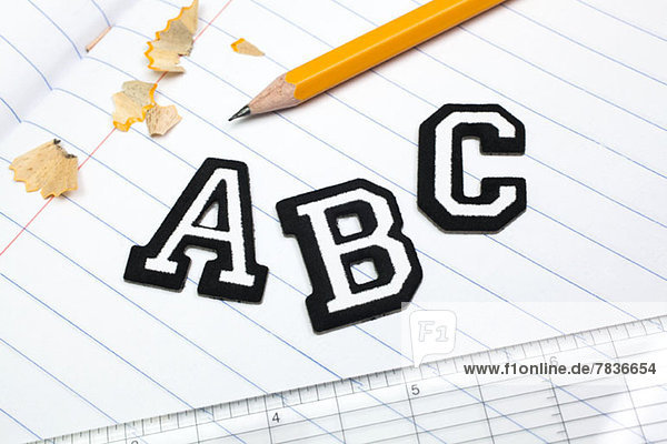 Varsity Schriftaufkleber  die A  B  C auf einem gefütterten Notizbuch mit Lineal und Bleistift buchstabieren.