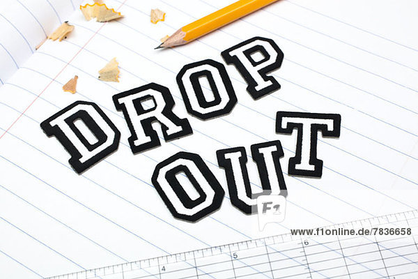 Varsity-Fontsticker buchstabieren Dropout auf einem gefütterten Papiernotizbuch mit Lineal und Bleistift