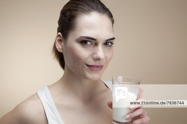 Eine lächelnde junge Frau hält ein Glas Milch.