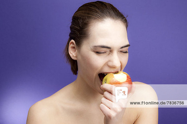 Eine junge Frau beißt gierig in einen Apfel.