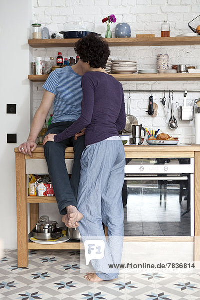 Ein altersgemischtes Paar  das sich in seiner Küche küsst.