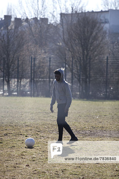 Ein junger Mann tritt einen Fußball in einem Stadtpark.
