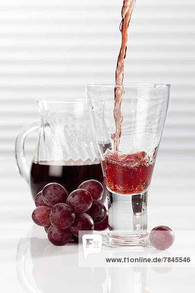 Karaffe und Glas mit gießendem roten Traubensaft  Nahaufnahme