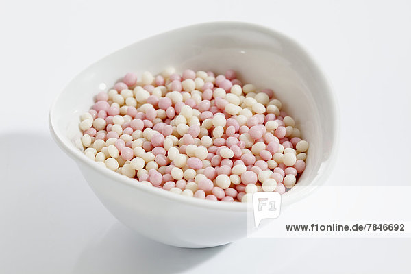 Bowl of pink and white crispies on white background  close up