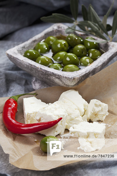 Schale mit grünen Oliven in Olivenöl mit Schafskäse und Chili auf Textil  Nahaufnahme