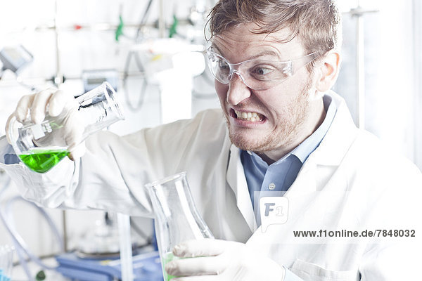 Germany  Young scientist pouring green liquid into erlenmeyer flask