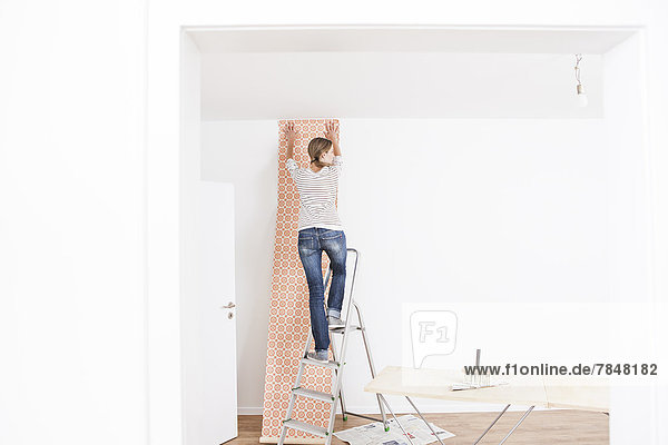 Woman sticking wallpaper on wall