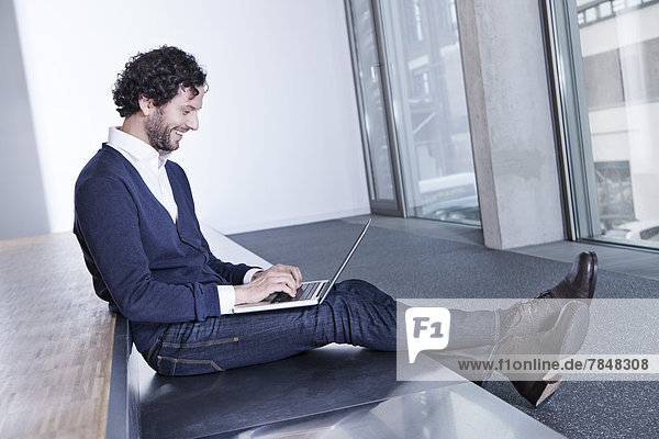 Germany  North Rhine Westphalia  Cologne  Businessman using laptop  smiling