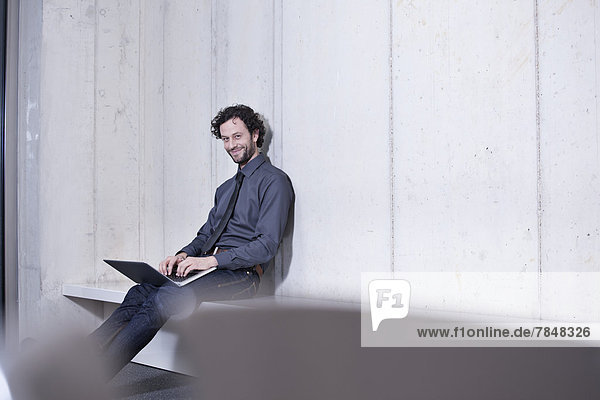 Deutschland  Nordrhein-Westfalen  Köln  Portrait eines Geschäftsmannes mit Laptop  lächelnd