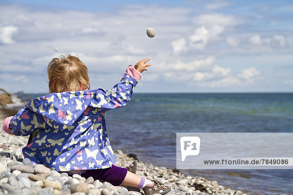 Dänemark  Mädchen sitzt am Strand  wirft Stein ins Meer