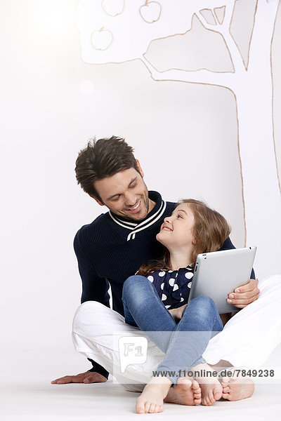 Vater und Tochter sitzend und mit digitalem Tablett,  lächelnd