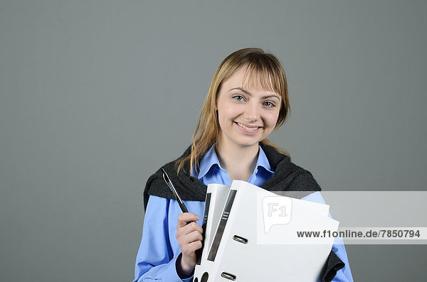 Porträt einer jungen Geschäftsfrau mit Stift und Mappe  Praktikantin  lächelnd