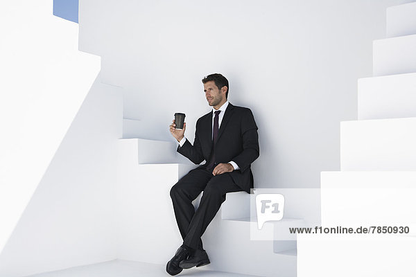 Geschäftsmann im schwarzen Anzug mit Kaffeetasse auf der Treppe sitzend
