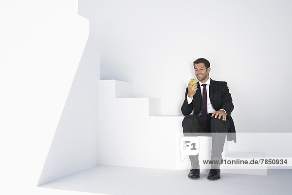 Geschäftsmann im schwarzen Anzug sitzend auf einer Treppe mit Apfel  lächelnd
