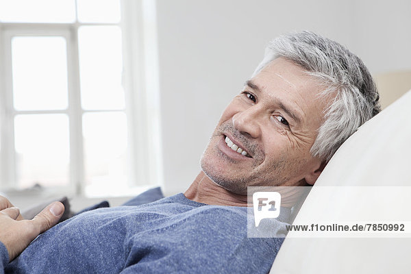 Porträt eines reifen Mannes  der sich auf dem Sofa entspannt  lächelnd