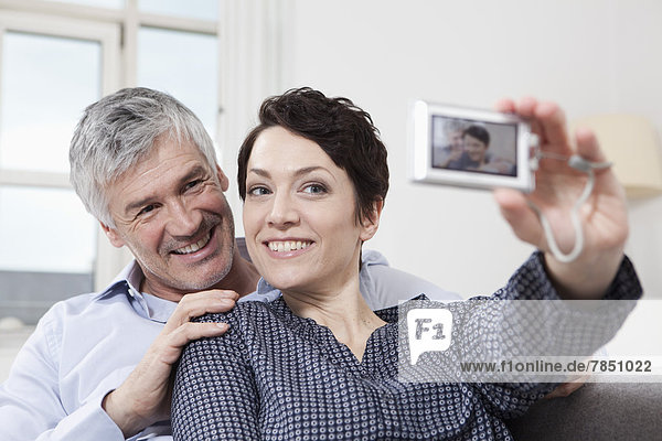 Germany  Bavaria  Munich  Couple taking self portrait of themselves at home  smiling