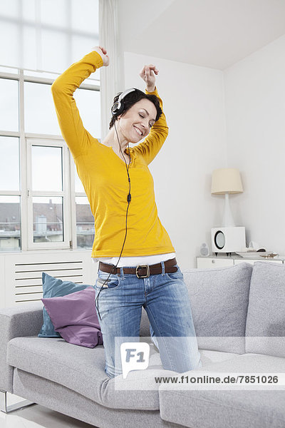 Mittlere erwachsene Frau  die Musik auf der Couch hört  lächelnd