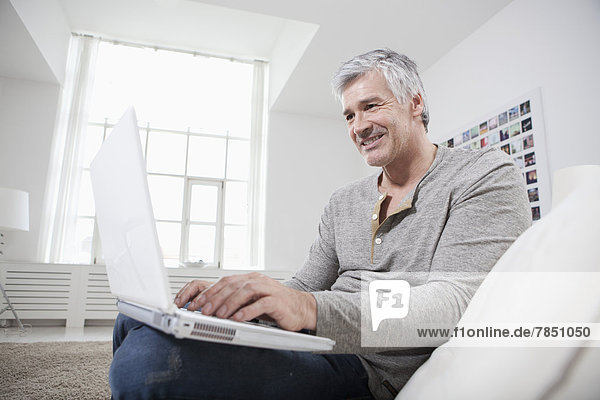 Mature man using laptop on couch  smiling