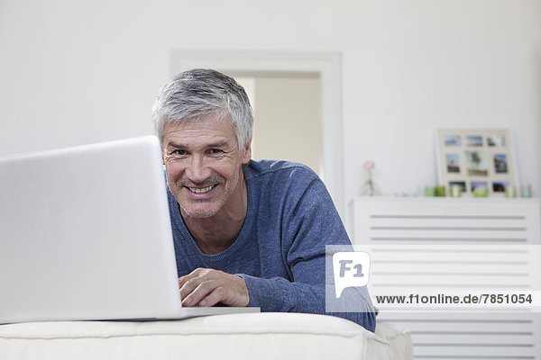 Portrait of mature man using laptop on couch  smiling
