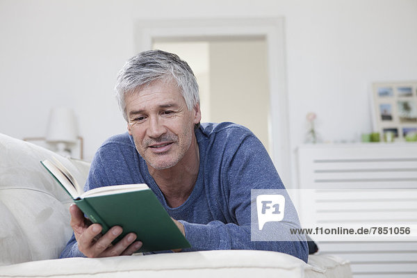 Erwachsener Mann liest Buch auf der Couch  lächelnd
