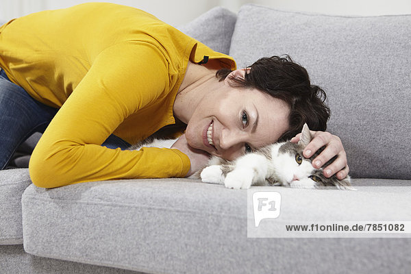 Mittlere erwachsene Frau mit Katze auf der Couch  lächelnd