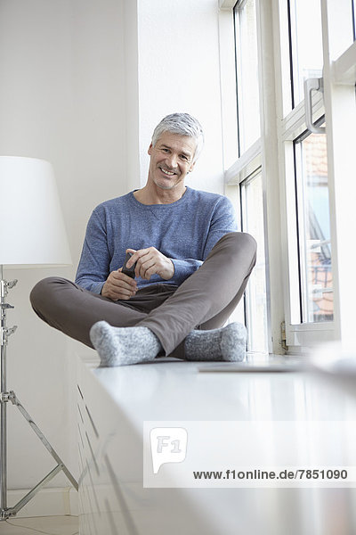 Portrait of mature man sitting at window  smiling