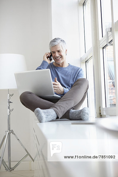Erwachsener Mann spricht auf dem Handy und mit dem Laptop  lächelnd