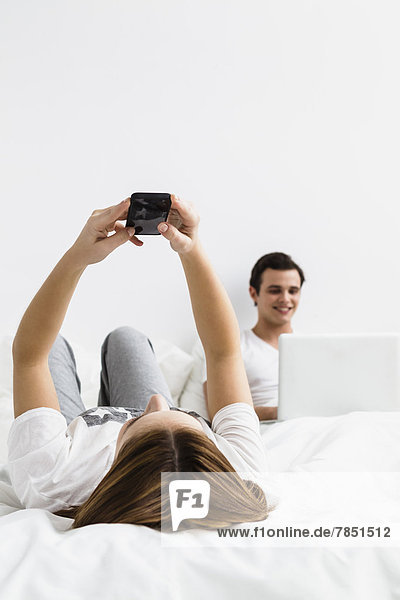 Young woman with mobile phone while young man using laptop in background  smiling