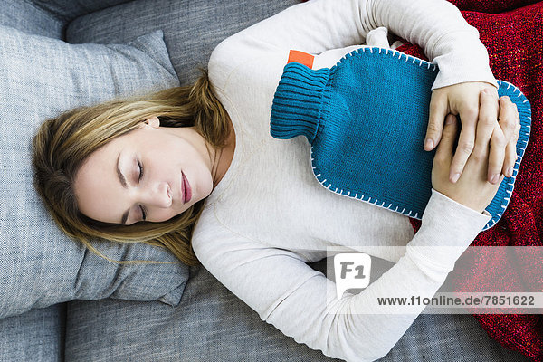 Junge Frau schläft auf Couch mit Wärmflasche