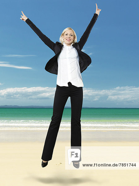 Porträt einer Geschäftsfrau  die am Strand springt  lächelnd