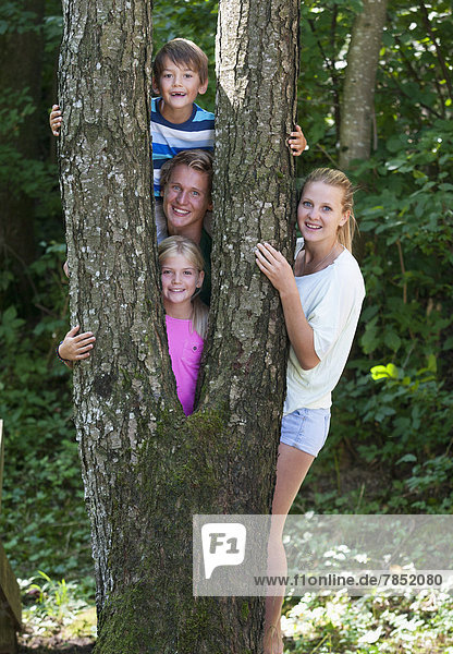 Österreich  Portrait von Freunden  die hinter einem Baumstamm stehen  lächelnd