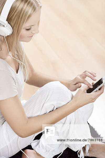 Young blond woman with smartphone and headphones at home