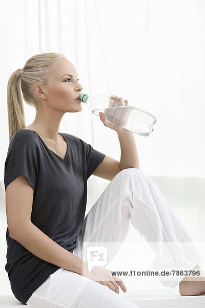 Junge blonde Frau trinkt aus einer Wasserflasche