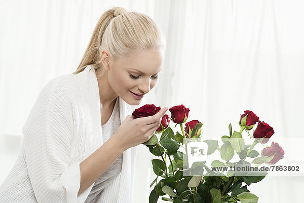 Junge blonde Frau riecht an Rosenstrauß
