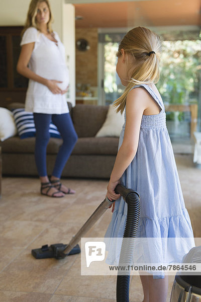 Little girl vacuuming  pregnant mother in background