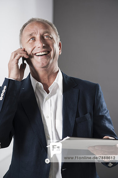 Smiling mature businessman using smartphone and digital tablet