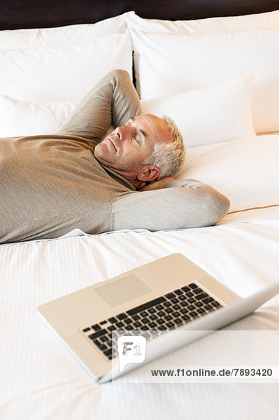 Man resting on the bed with a laptop in a hotel room