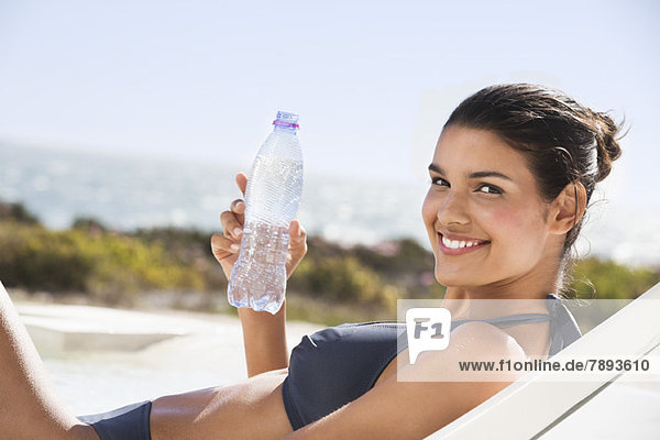 Schöne Frau mit einer Wasserflasche beim Sonnenbaden am Strand
